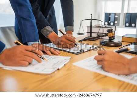 A team meeting of business people and a lawyer in formal suits is taking place at a desk, discussing a contract and various aspects of the law and litigation.