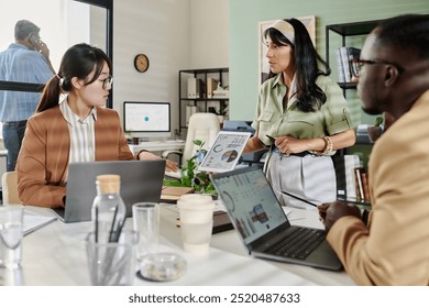 Team members collaborating on project details in office setting, with laptops and visual aids enhancing presentation impact - Powered by Shutterstock