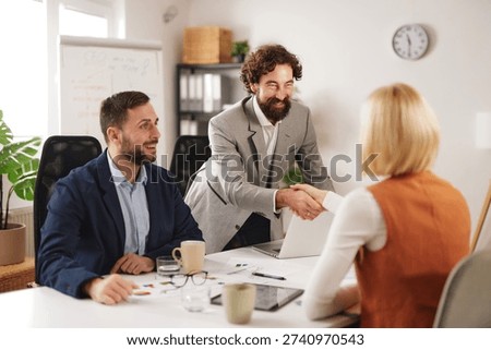 Team members engage in discussion while one person shakes hands with another, showing collaboration and teamwork in a modern office setting.