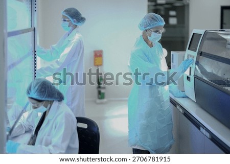 A team of microbiologists processes samples in a sterile biotech facility. They use laminar flow hoods and automated analyzers for pharmaceutical research and pathology diagnosis.