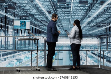 Team of microchip designers checking equipment malfunctions in industry 4.0 manufacturing plant with tablet. Female manager and colleague working together to assess smart factory semiconductor yields