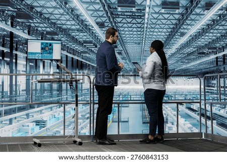 Team of microchip designers checking equipment malfunctions in industry 4.0 manufacturing plant with tablet. Female manager and colleague working together to assess smart factory semiconductor yields