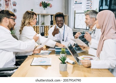 Team of Multicultural doctors sitting at table on conference room and sharing with reports during medical research. African American smiling doctor showing thumb up at camera