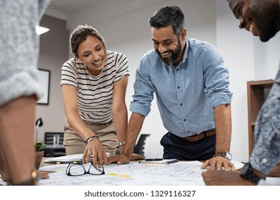 Team of multiethnic architects working on construction plans in meeting room. Engineers discussing on project in office. Mature businessman and woman standing around table working on blueprint.
