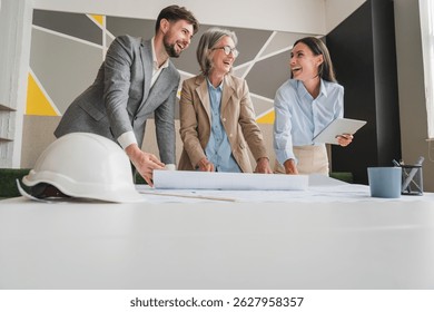 Team of multiethnic architects working on construction plans in meeting room. Engineers discussing on project in office. Businesswoman and her colleagues standing around table working on blueprint.