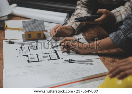 Team of multiethnic architects working on construction plans in meeting room. Engineers discussing on project in office. Mature businessman and woman standing around table working on blueprint.
