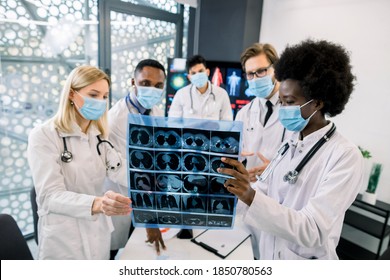 Team of multiethnic doctors or scientists, wearing protective medical face masks, looking at the CT scan of the patient and discussing the results of new treatment or clinical trial. Focus on CT image - Powered by Shutterstock