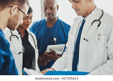 Team of multiracial doctors standing reading patient records on a ward round in a hospital, close up view of diverse men and women