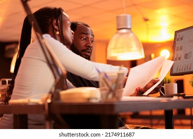 Team of office employees working together on paperwork report, doing research to create project data on computer. Analyzing documents with charts, doing teamwork collaboration during sunset. - Shutterstock ID 2174911687