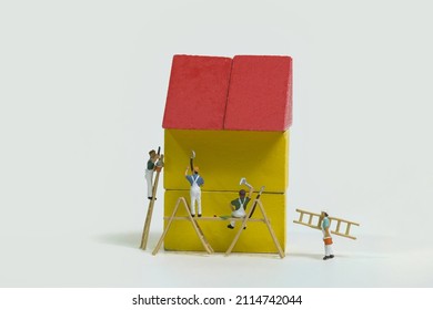 A Team Of Painters With Wooden Ladder And Scaffolding Is Painting A Yellow House With A Red Roof