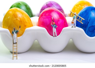 A Team Of Painters With A Wooden Ladder And Scaffolding Is Painting Chicken Eggs Lying In A Cup. White Background