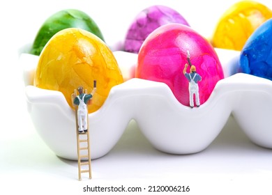 A Team Of Painters With A Wooden Ladder And Scaffolding Is Painting Chicken Eggs Lying In A Cup. Closeup, White Background