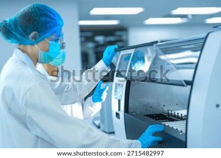 A team of pathologists processes samples using an automated staining machine. They are conducting pharmaceutical research or diagnostic testing in a sterile biotech lab.
