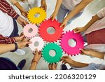 Team of people connecting gears. Cropped shot group of young men and women standing in circle and joining colorful cogs together. Teamwork, integration, business, education, success concept background