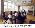 Team of people having class with business trainer. Group of male and female employees sitting at desks in modern office and listening to lecture by experienced teacher sharing knowledge and guidance
