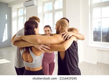 Team Of People Hugging At The Gym. Happy, Cheerful, Smiling, Supportive Friends Standing In A Circle With Their Arms Around Each Other's Shoulders. Fitness Workout, Gym Buddy Group, Motivation Concept