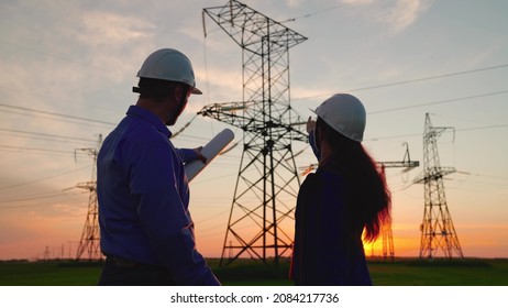 Team of power engineers construction workers, woman, man work together on the construction of power towers. Teamwork and engineers, partners shaking hands, good work. Electricians in protective helmet