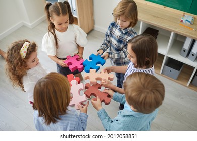 Team of primary school children or kindergartners standing in circle join pieces of colorful jigsaw puzzle, high angle close up. Education, learning, engaging activities in classroom, teamwork concept - Powered by Shutterstock