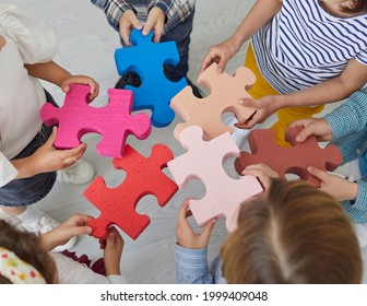 Team Of Primary School Children Standing In Circle Join Pieces Of Colorful Jigsaw Puzzle, Top View High Angle View From Above Close Up. Teamwork, Education, Learning Activities In Classroom Concept