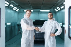 Team Of Professional Automotive Painting Technician In Chemical Protecting Suit Standing In Front Of The Painting Chamber Together. Car Painting And Detailing Technicians Portrait.