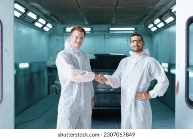 Team of professional automotive painting technician in chemical protecting suit standing in front of the painting chamber together. Car painting and detailing technicians portrait.