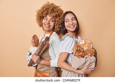 Team of professional bakers pose with crusty freshly baked bread stand backs to each other hold rolling pin wear aprons isolated over brown studio background work in bakehouse. Bakery concept - Shutterstock ID 2249680279