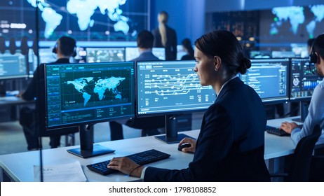 Team Of Professional Computer Data Science Engineers Work On Desktops With Screens Showing World Map, Charts, Graphs Infographics Technical Business Data And Statistics. Dark Control Monitoring Room.