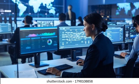 Team Of Professional Computer Data Science Engineers Work On Desktops With Screens Showing Charts, Graphs, Infographics, Technical Business Data And Statistics. Dark Control And Monitoring Room.
