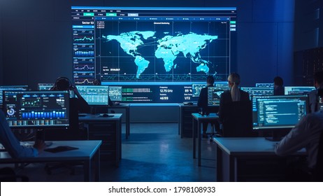 Team Of Professional Computer Data Science Engineers Work On Desktops With Screens Showing Charts, Graphs, Infographics, Technical Neural Network Data And Statistics. Dark Control And Monitoring Room.