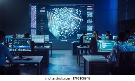 Team Of Professional Computer Data Science Engineers Work On Desktops With Screens Showing Charts, Graphs, Infographics, Technical Neural Network Data And Statistics. Dark Control And Monitoring Room.