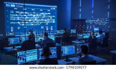 Team of Professional Computer Data Science Engineers Work on Desktops with Screens Showing Charts, Graphs, Infographics, Technical Neural Data and Statistics. Low Key Control and Monitoring Room.