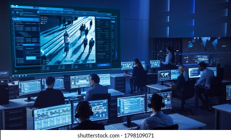 Team Of Professional Cyber Security Data Science Engineers Work On Surveillance Tracking Shot Of People Walking On City Streets. Big Dark Control And Monitoring Room With Computer Displays.