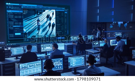 Team of Professional Cyber Security Data Science Engineers Work on Surveillance Tracking Shot of People Walking on City Streets. Big Dark Control and Monitoring Room with Computer Displays.