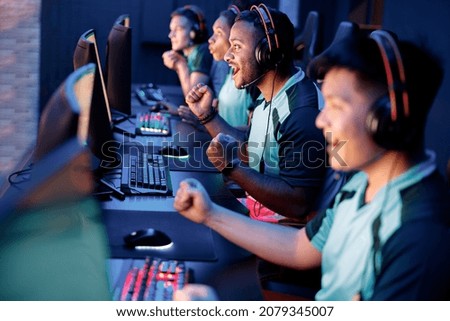 Team of professional esport gamers with happy man in focus playing in video games on cyber games tournament indoors