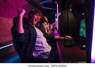 Team of professional gamers wearing headphones celebrating victory while playing online video game on tournament in modern cybersport club