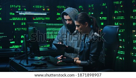 Team of professional hackers using computer for organizing massive data breach attack. Secret location surrounded by displays and servers.