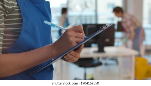 Team of professional janitors in uniform cleaning office. Close up of woman cleaner checking list on clipboard supervising cleaning service team work in modern office - Shutterstock ID 1904169550