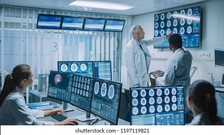 Team of Professional Medical Scientists Work in the Brain Research Laboratory. Neurologists / Neuroscientists Surrounded by Monitors Showing CT, MRI Scans Having Discussion and Working on PC