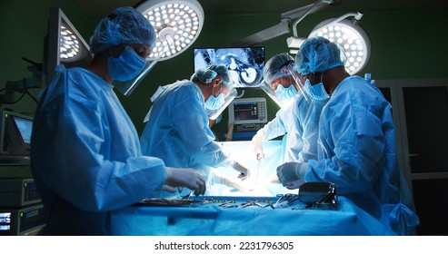 Team of professional mixed-races doctors and assistants in medical uniforms performs heart transplant operation under lamp using medical tools in operating room looking at monitor. Surgery concept - Powered by Shutterstock