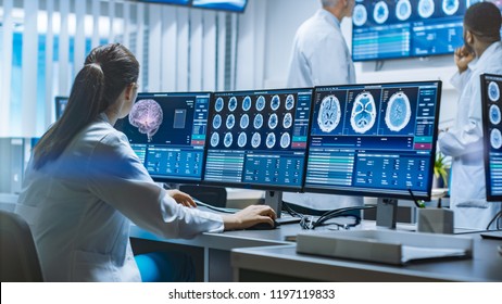 Team Of Professional Scientists Work In The Brain Research Laboratory. Neurologists / Neuroscientists Surrounded By Monitors Showing CT, MRI Scans Having Discussions And Working On Personal Computers.