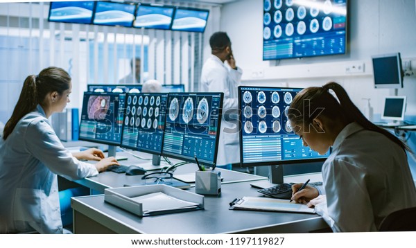 Team of Professional Scientists Work in the\
Brain Research Laboratory. Neurologists / Neuroscientists\
Surrounded by Monitors Showing CT, MRI Scans Having Discussions and\
Working on Personal\
Computers.