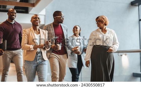 Team of professionals engaging in a conversation while walking through a brightly lit office corridor. They exhibit a sense of companionship and happiness, indicative of a positive workplace culture.
