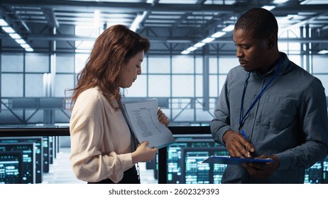 Team of IT professionals looking over data center checkup checklist paperwork. African american man and colleague collaborating in server farm reading documentation files, camera B
