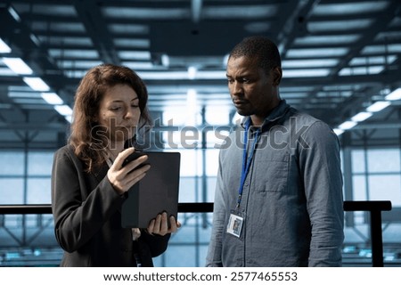Team of programmers in data center using automation tools on tablet. IT professional and colleague ensuring continuous uptime of server farm, managing data flows with device