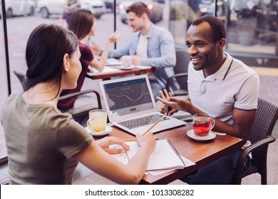 Team project. Cheerful merry two colleagues working at cafe while preparing project and woman noting ideas - Shutterstock ID 1013308282