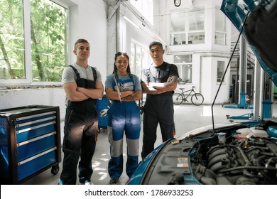 Team of proud diverse mechanics in uniform, two men and a woman smiling at camera while standing at auto repair shop. Car service, repair, maintenance and people concept. Horizontal shot