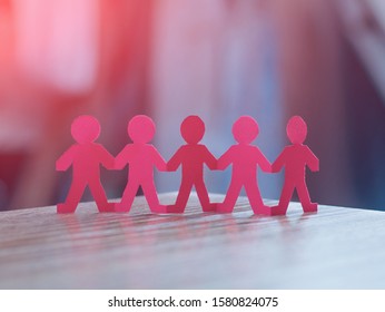 Team Of Red Paper Chain People In A Row On Blurred Background Holding Hands