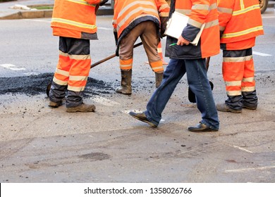 A team of road builders collect and align fresh asphalt with a shovel along the repaired part of the road. - Shutterstock ID 1358026766