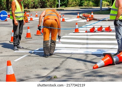 A team of road workers on a fenced section of the carriageway with a paint sprayer mark white road markings for a pedestrian crossing. Copy space.