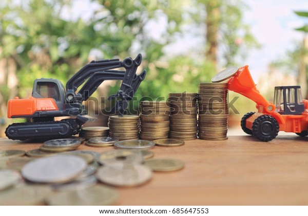 Team and saving concept, loader\
and construction car help put coins in stair step roll to top on\
wood table, natural green bright light background, blur\
money